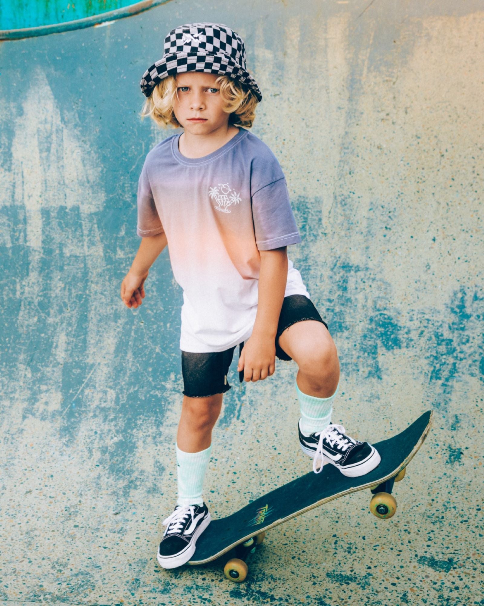 Alphabet Soup's Kids Venice Dip Dye Tee for boys aged 8 to 16. Featuring 100% Cotton Jersey, a box tee fit, and short sleeves. It comes in a Blue/Peach/White colourway with 3-colour dip dye and shaka prints on both chest and back.