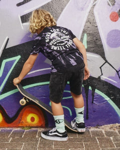   Kids Riptide Short Sleeve Tee by Alphabet Soup for boys aged 2-7. Crafted from 100% cotton jersey, this regular fit tee features short sleeves, a ribbed crew neckline, a straight hemline, and a two-tone diagonal purple and black tie dye. Plus, it has printed retro surf graphics to chest and back featuring “Here For The Swell Times”.